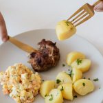 From above of crop anonymous person with cutleries eating delicious fried cutlet and hot boiled potatoes with parsley garnished with nutritious Russian salad