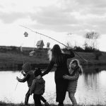 A mother and her children enjoy a serene moment at a lakeshore, captured in black and white.